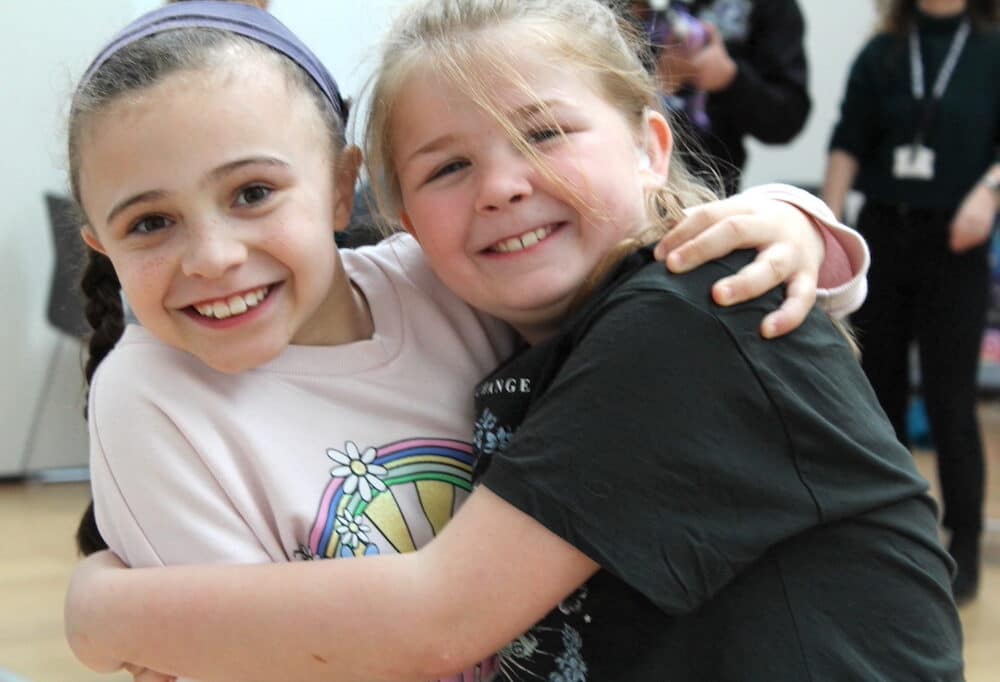 Two girls hug and smile at the camera.