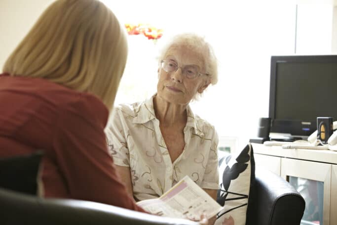 Two ladies, one older, sit talking in an office space.