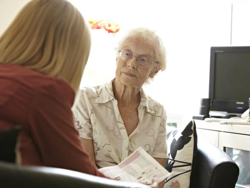Two ladies, one older, sit talking in an office space.