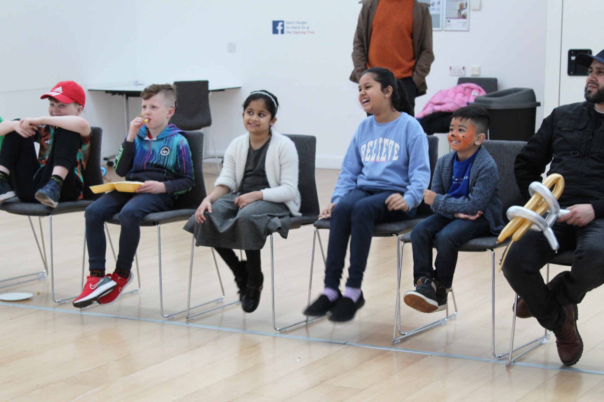 Five children sit watching someone offscreen smiling and laughing.