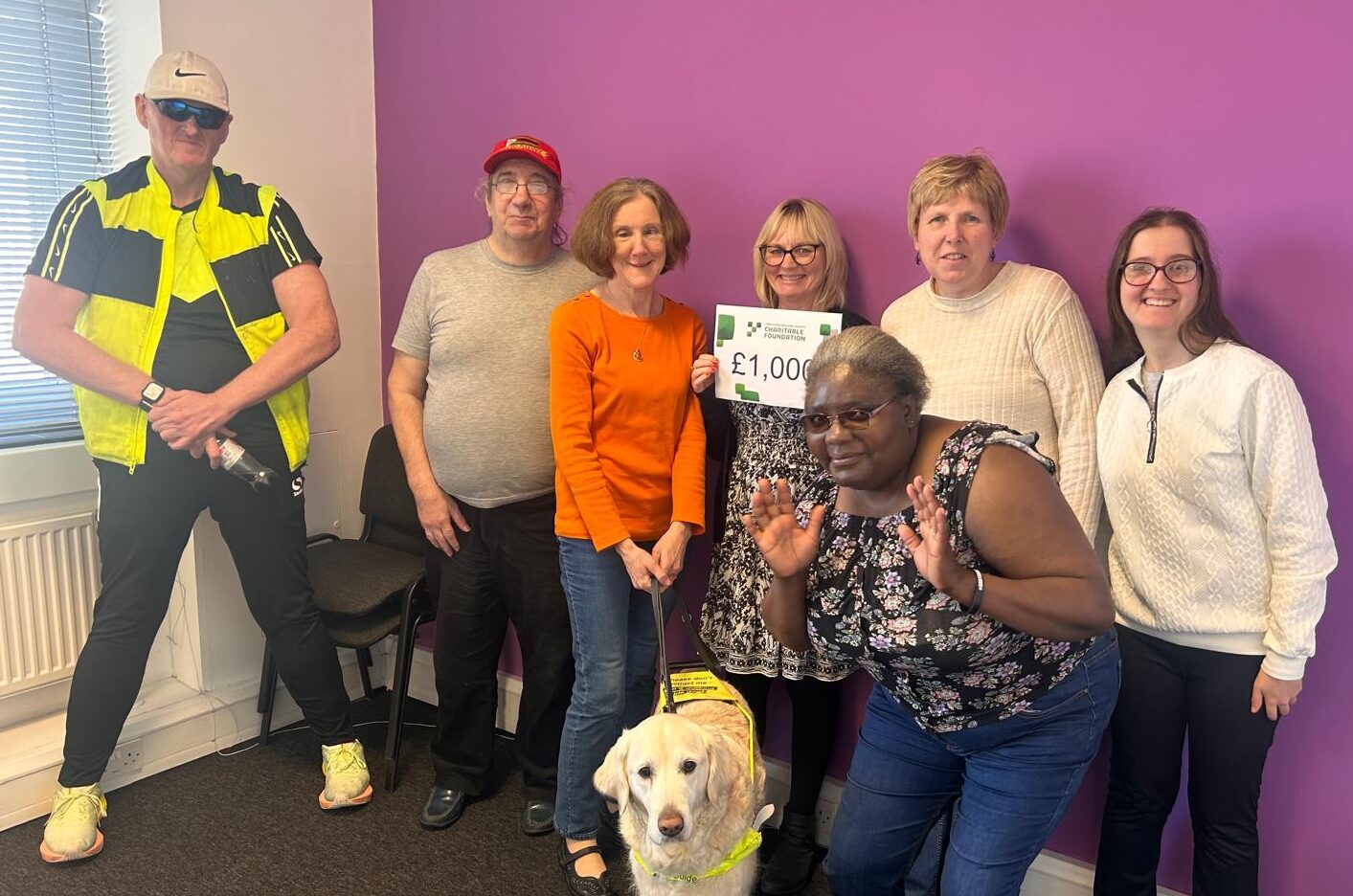 The art group facing the camera and smiling. Middle person holds a piece of paper which says £1,000