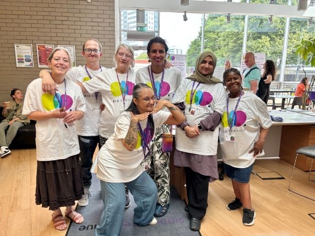6 women and 1 man are huddled together, smiling towards the camera for a group photo. They are all wearing white t-shirts with our BID logo in the centre.