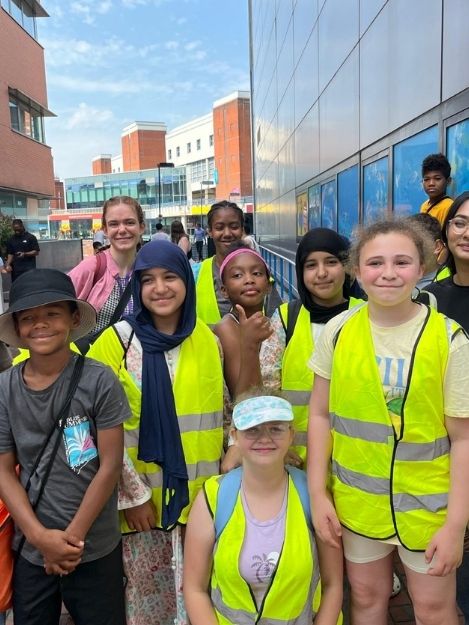 Staff and children of mixed ages stood together outside an aquarium smiling at the camera with most wearing high visibility vests.