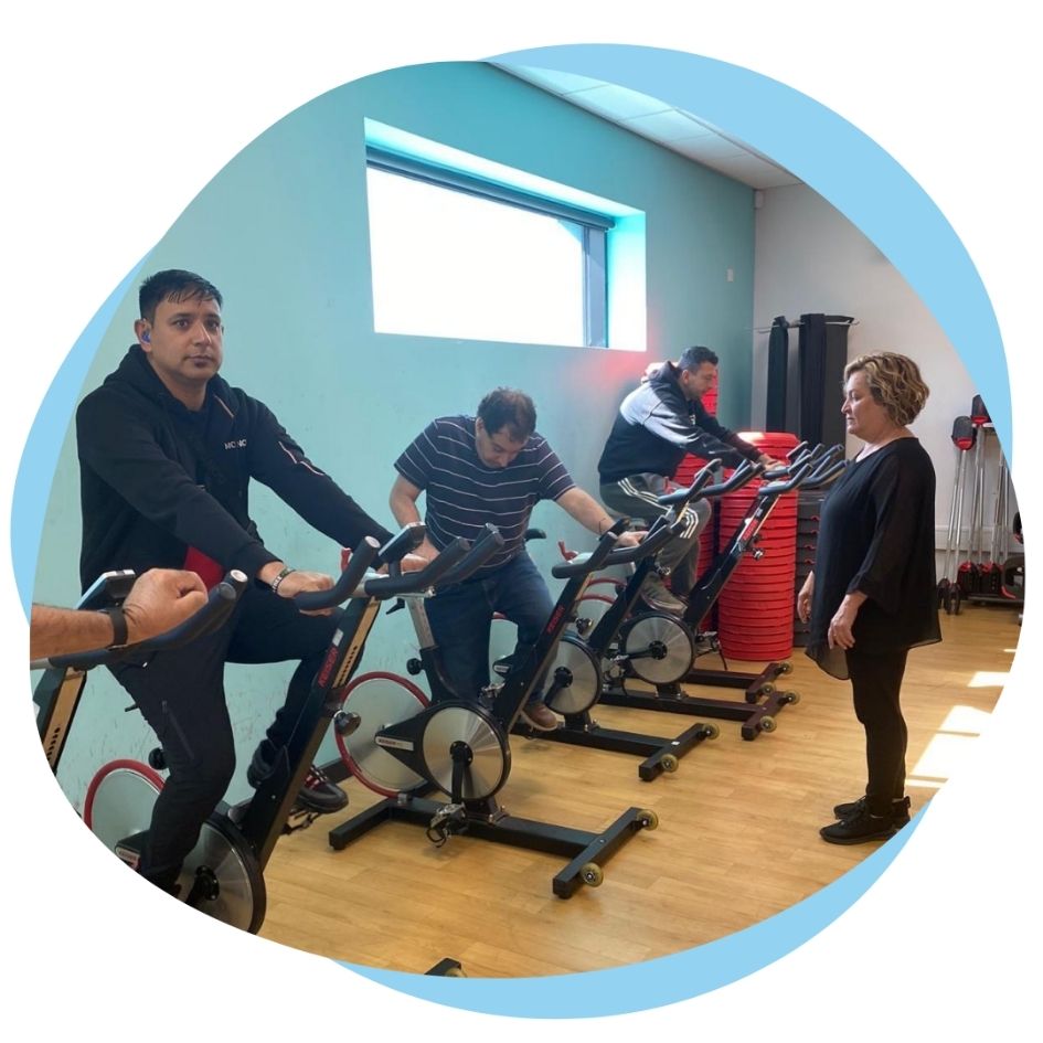 3 men are on stationary exercise bikes in a gym.