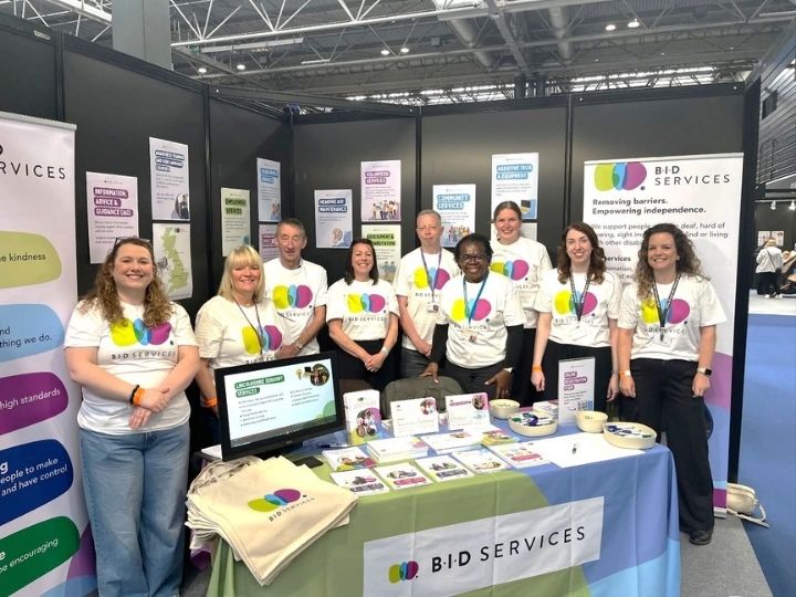 Staff stood together, smiling behind the BID Services set up for DeafEXPO. In order: Kim, Jayne, Ian, Alex, Jock, Pauline, Vanessa, Beth and Jo.