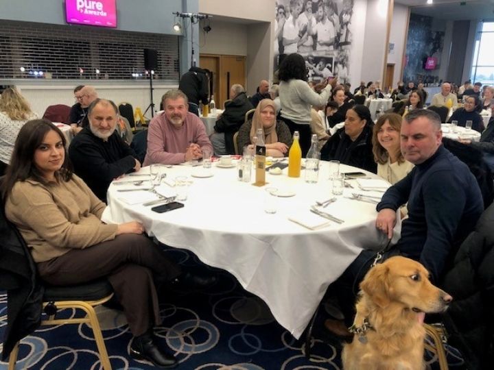 Group photo of 7 employment team members seated at a table with guide dog, Ned.