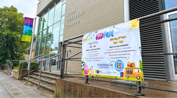 Deaf Cultural Centre building which is 2 stories tall, with light grey bricks and large windows. Focus in on the BID Fest decorative banner.