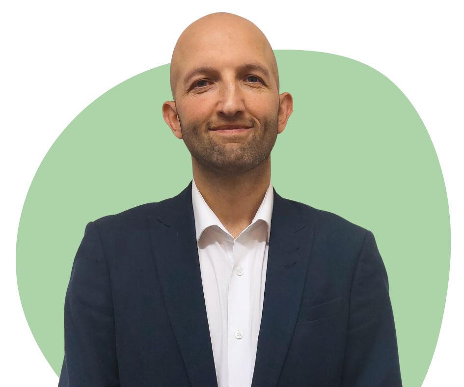 White bald man with stubble against a green background.