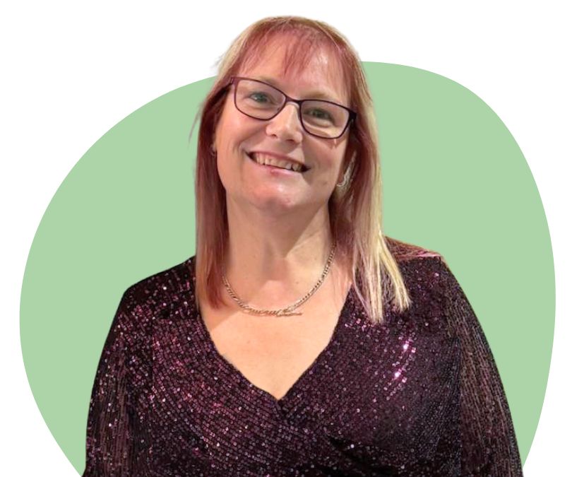 White woman with shoulder length blonde and purple hair with glasses against a green background.