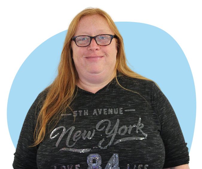 White woman with long red hair and glasses against a blue background.