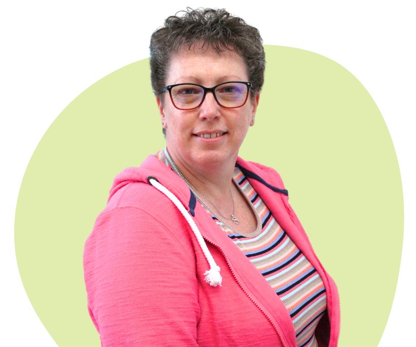 White woman with short dark grey hair and glasses against a green background.