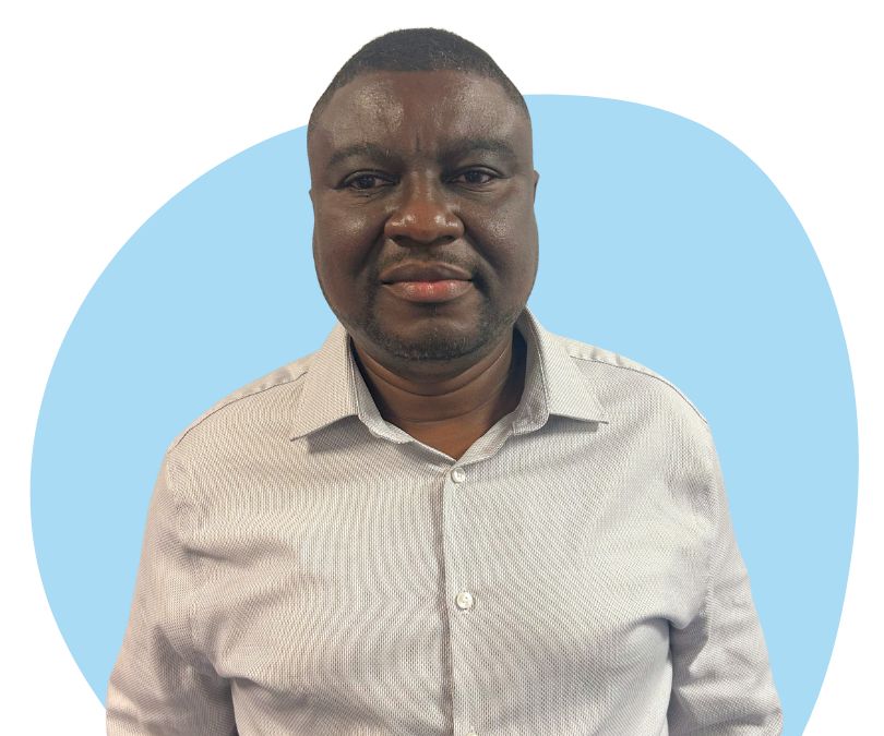 A black man with short black hair and stubble against a light blue background.