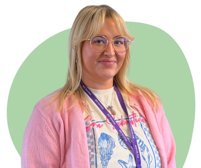 A white woman with long blonde hair and glasses, against a dark green background.
