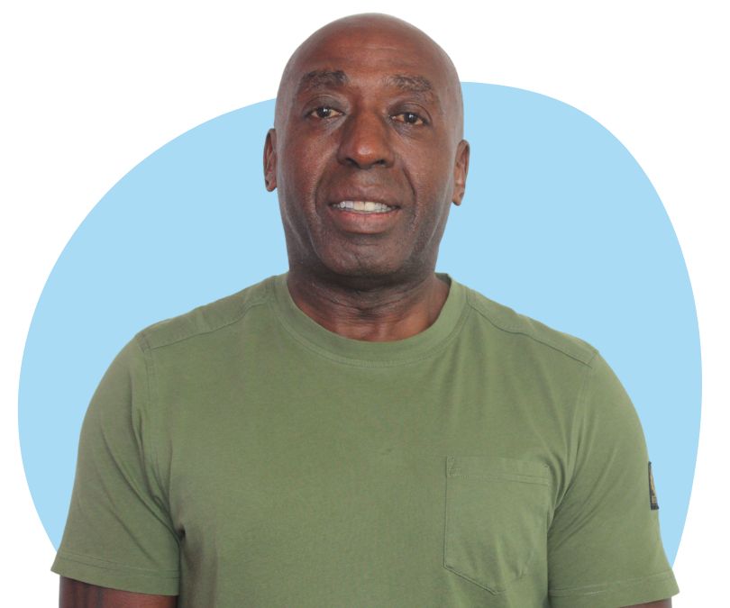 Black bald man with stubble against a blue background.