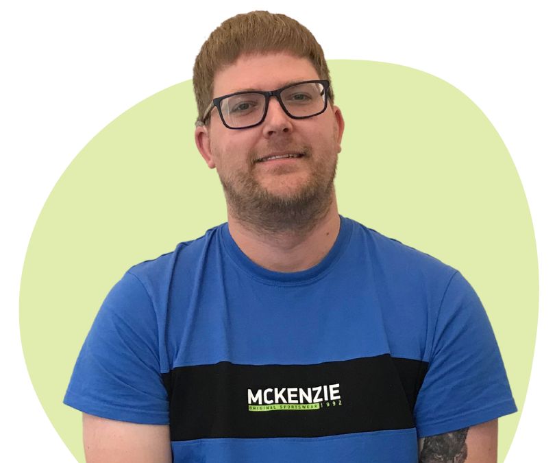 White man with short dark blonde hair and glasses against a green background.