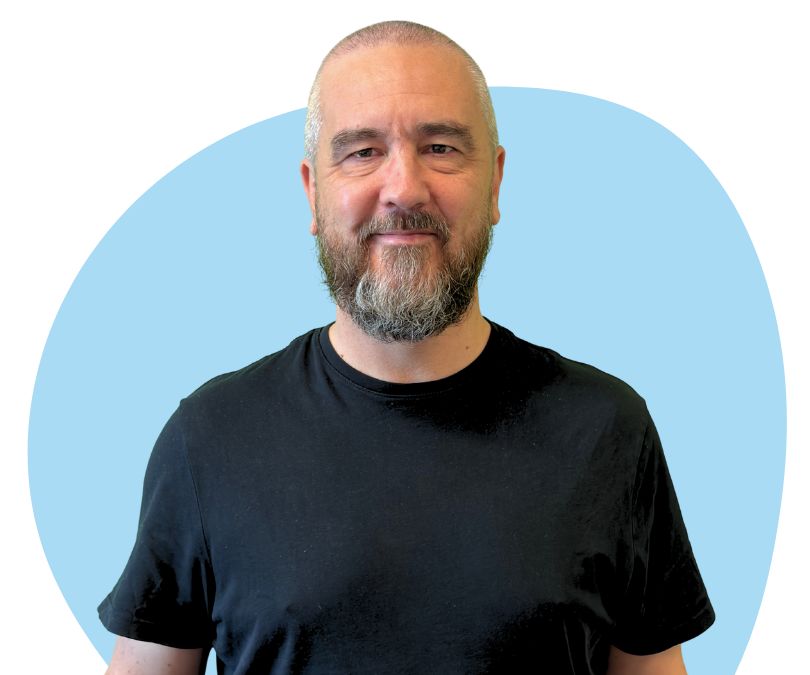 White man with short grey hair and beard against a blue background.