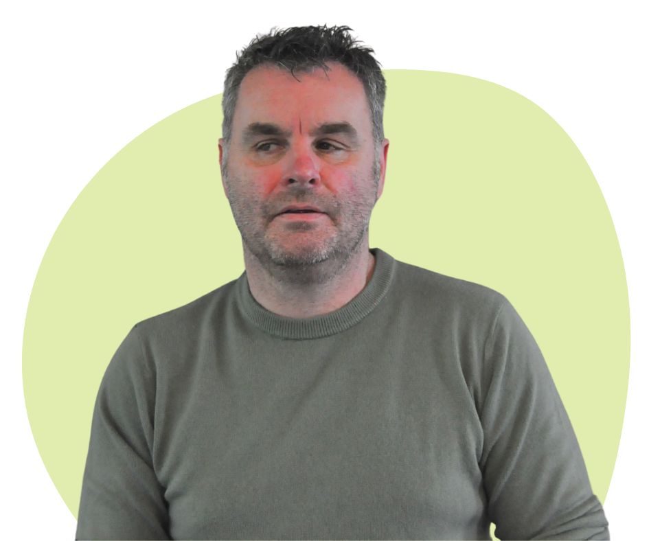 White man with short dark grey hair and stubble against a green background.