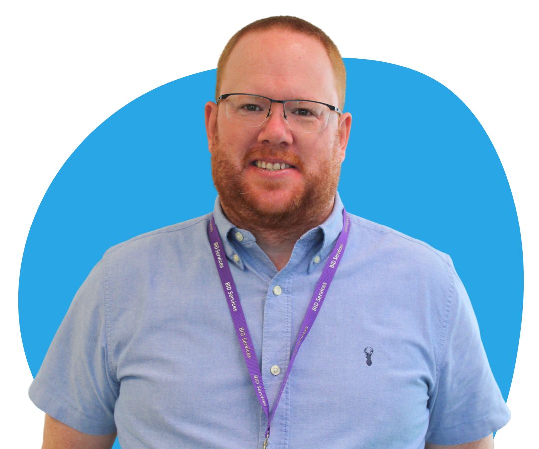 White man with short ginger hair, a beard and glasses against a light blue background.