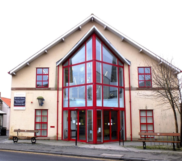 A two story building with beige walls. The windows and doors are red-framed.