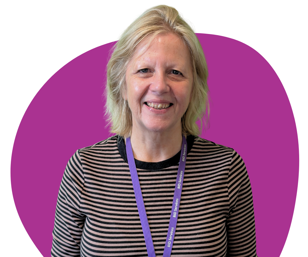 A white woman with shoulder length blonde hair against a purple background.