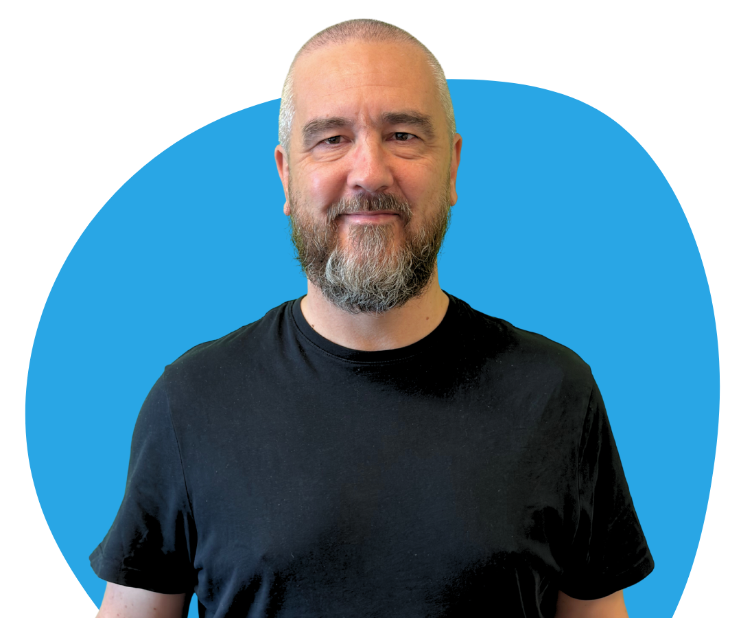 A white man with short grey hair and a beard against a light blue background.