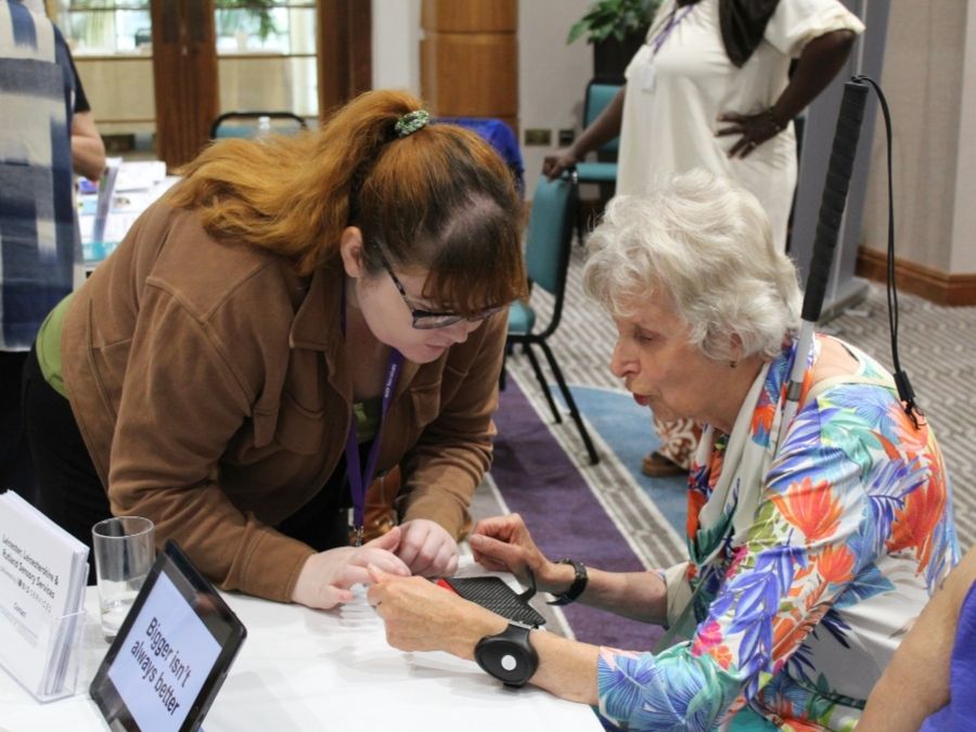 A woman is leaning down close to an elderly woman while they look at tech together.