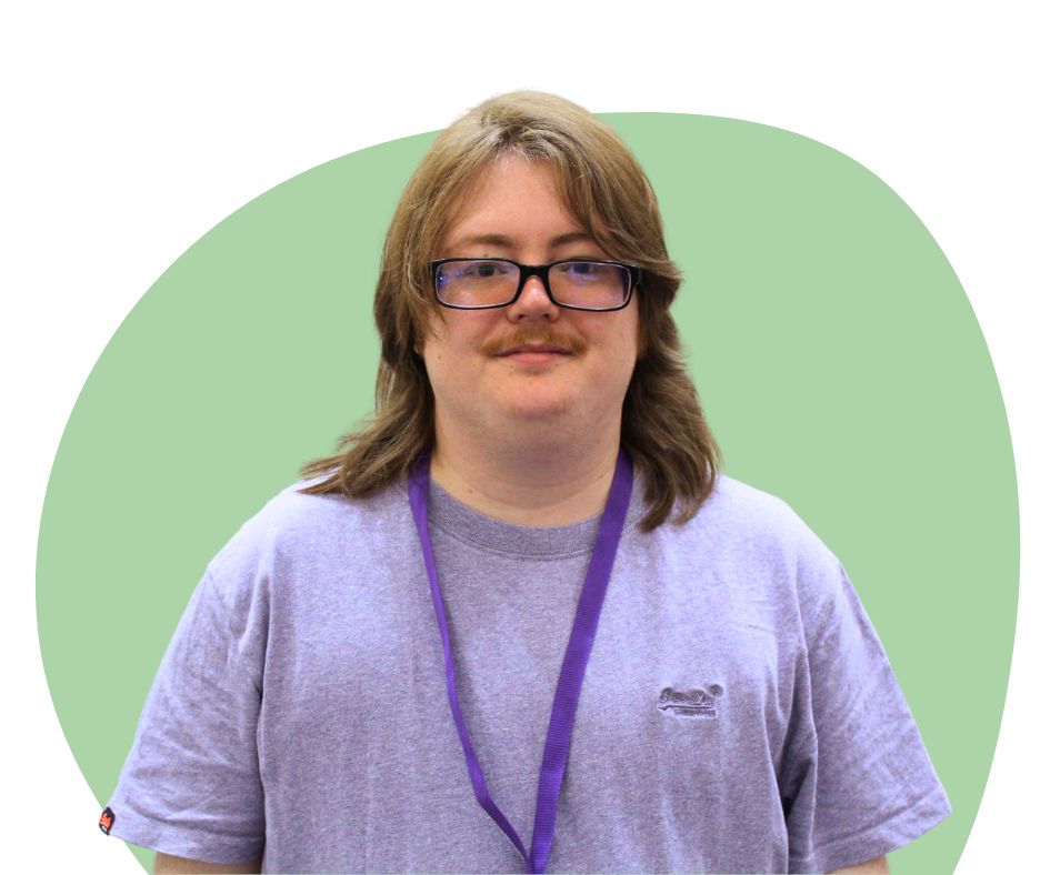 A while male with shoulder length strawberry blonde hair and black framed glasses against a dark green background.
