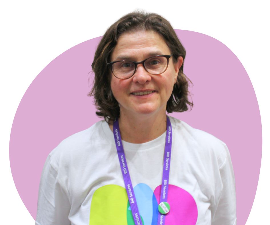 White woman with chin length dark brown hair and black framed glasses against a light purple background.